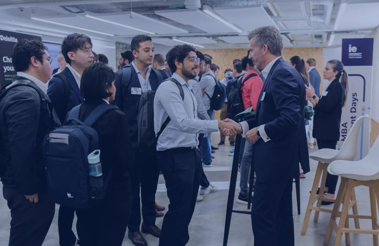 A group of professionally dressed people engaging in conversation and handshakes at a networking event.