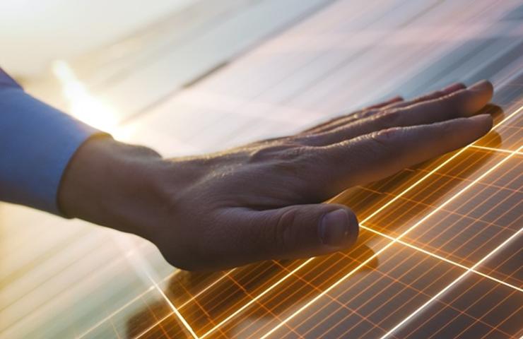 A hand gently touching a solar panel during sunset.