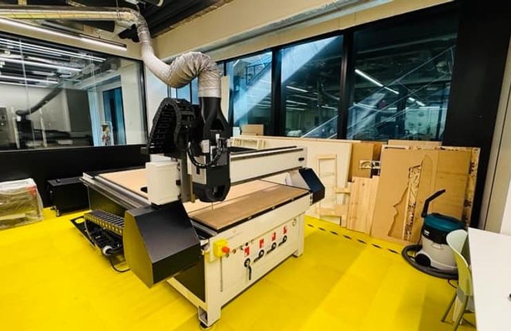 A modern CNC machine in a workshop setting with wooden materials in the background.