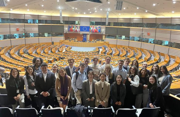 A group of people posing for a photo in a large auditorium with rows of seats and flags of various countries.