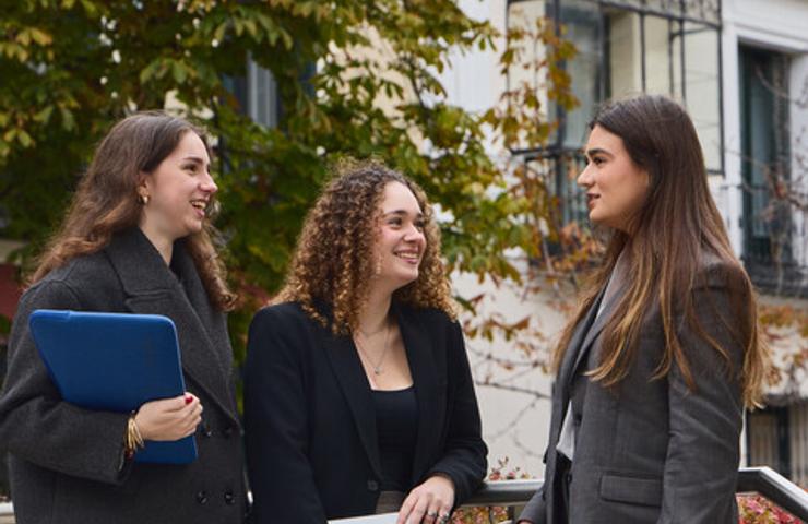 Three professionals are having a conversation outdoors in a city setting.