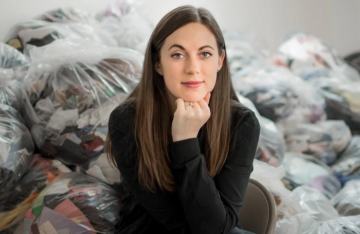 A woman seated in front of large plastic bags filled with assorted items.
