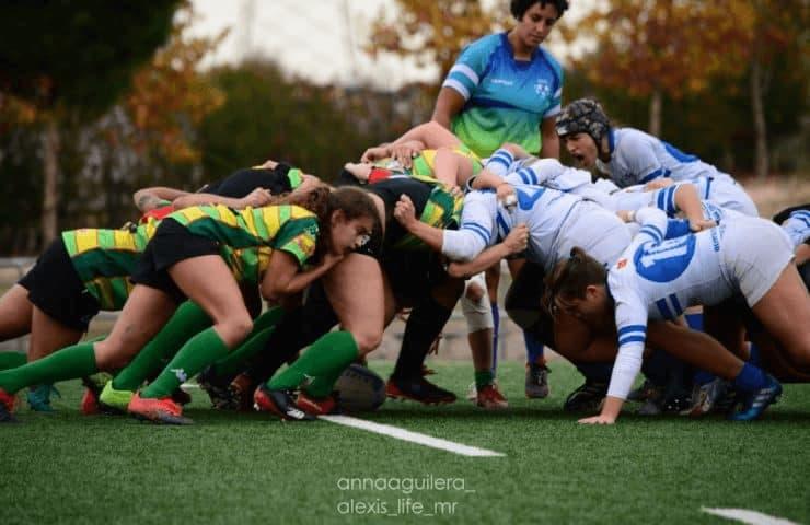 A women's rugby match showing two teams engaged in a scrum on a grass field.