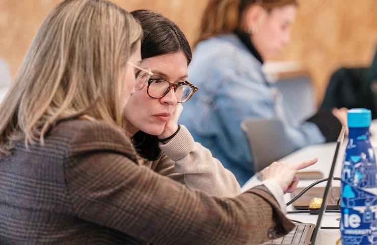 Two women are engaged in a focused discussion while working on a laptop.