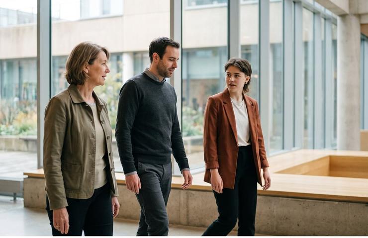 Three professionals are walking together in a modern office space.