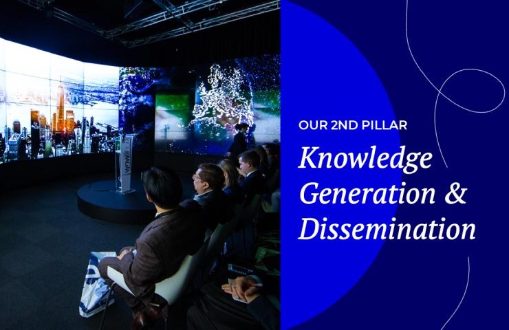 People watching a presentation on multiple screens in a darkened room, with text emphasizing 'Knowledge Generation & Dissemination'.