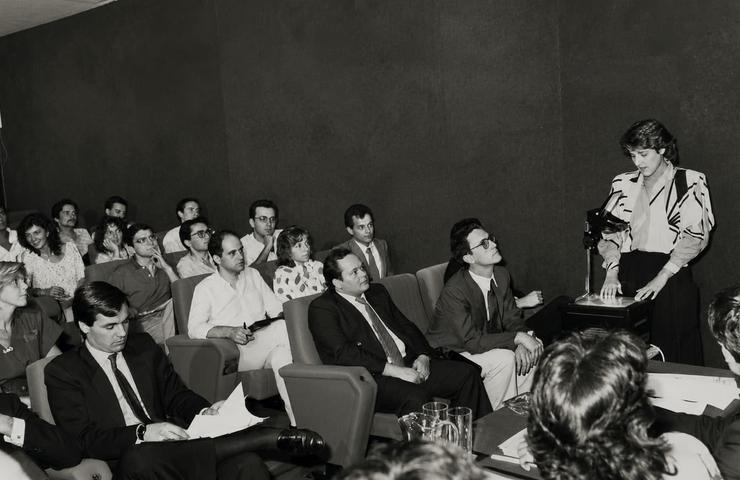 A woman presents in front of an audience during a meeting.