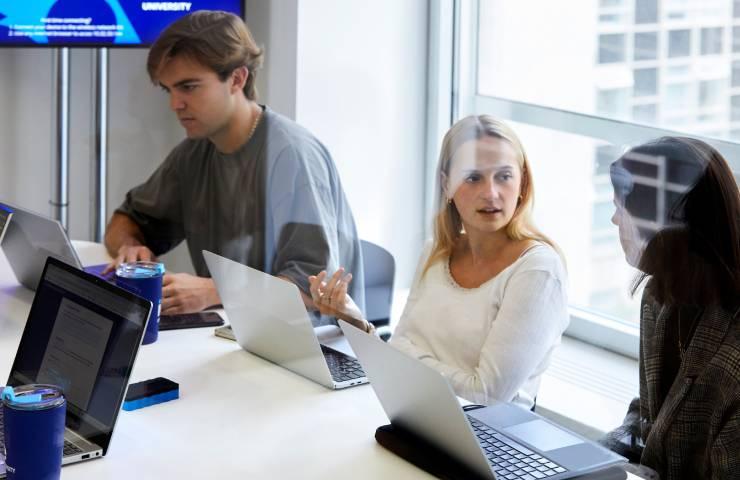 Three people, two women and one man, are working on laptops in a modern office environment.