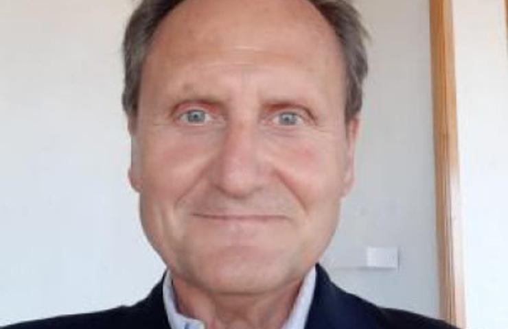 Portrait of a smiling elderly man in a suit jacket standing indoors.