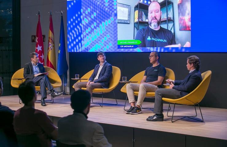 A panel discussion featuring several speakers and a video call participant.