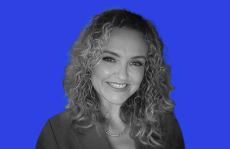 Black and white photo of a smiling woman with curly hair against a solid blue background.