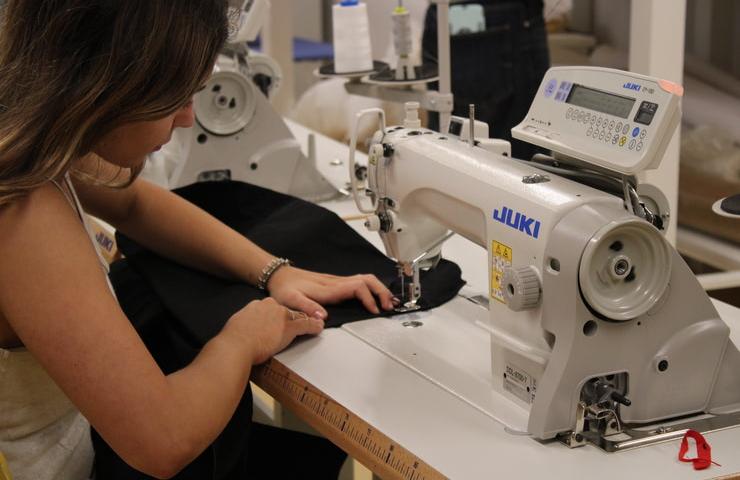 A woman attentively sewing fabric on a Juki sewing machine.