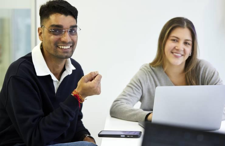 A man and a woman smiling and interacting at a table with a laptop.