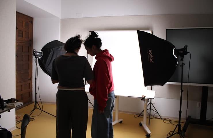 Two individuals are preparing for a photoshoot in a well-lit studio.