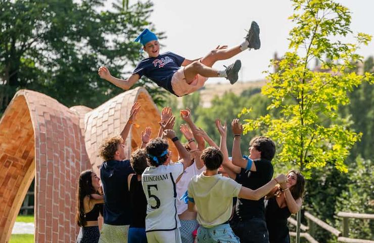 A group of young people joyfully catches a graduate being tossed in the air in a celebratory moment.