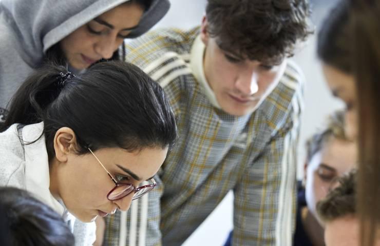 A group of young adults intently looks at something below the frame, possibly focusing on a project or discussion.