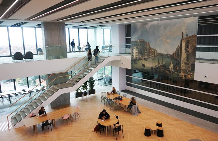 A modern indoor space featuring a large mural, a staircase, and people seated at tables.