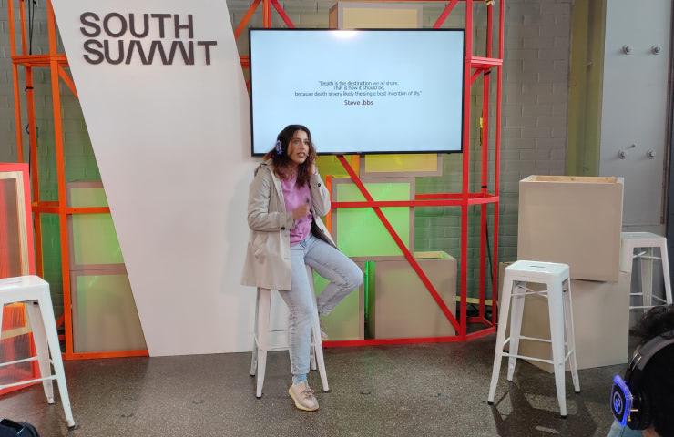 A woman is presenting at the South Summit event, standing next to a projected presentation.