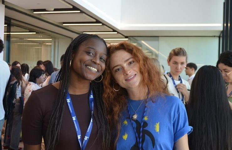 Two women smiling together at an event, with a crowd of people in the background.