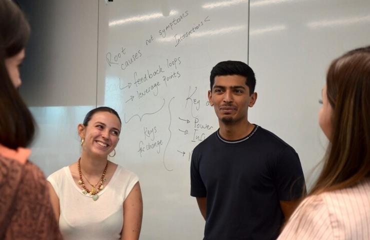 A group of individuals are engaged in a discussion in front of a whiteboard filled with notes.