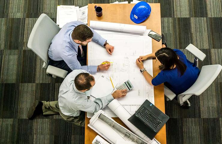 Three professionals analyzing architectural plans on a table in an office setting.