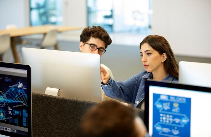 A young man and woman collaborate using computers in a modern office environment.