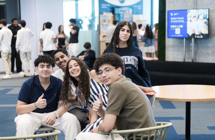 A group of five smiling students posing together in a modern indoor setting.