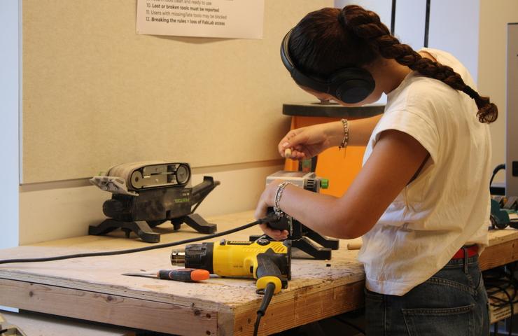 A woman is using a power drill in a workshop.