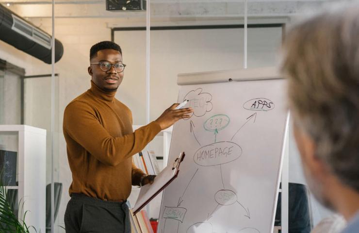 A man presenting a business strategy on a whiteboard to a colleague in a modern office