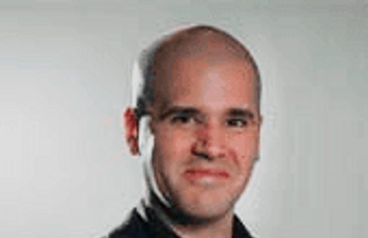 A portrait of a smiling bald man wearing a black shirt.