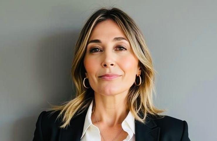 A professional woman wearing a black blazer and white shirt, smiling against a neutral background.