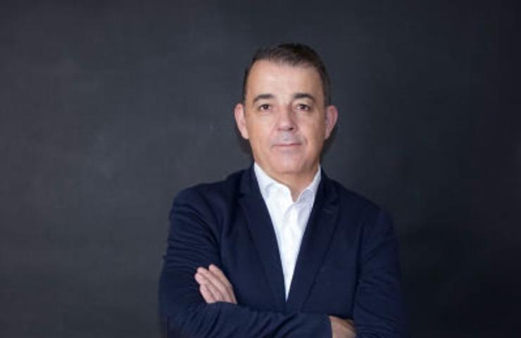 A professional portrait of a middle-aged man standing with arms crossed against a dark background.