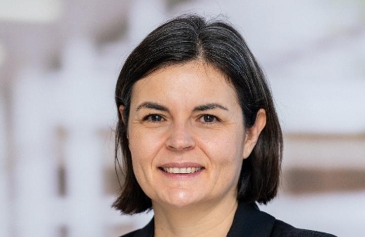 A professional portrait of a smiling woman with short, dark hair, wearing a black blazer over a white top.