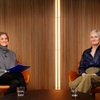Two women seated in stylish chairs engage in conversation on a modern set.