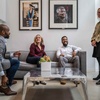 Four people, two men and two women, are having a lively conversation in a modern office lounge area.