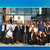 A large group of people gathered outdoors in front of a building with a promotional banner for AI4Gov accelerate program.