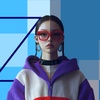 A woman with stylish glasses and a colorful outfit stands in front of a geometric background.