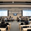 A group of people seated in a modern conference room with presentations displayed on screens.