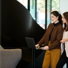Two women standing and using a laptop together in a modern office setting.