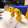 A toy robot with yellow legs and a blue body on a desk.