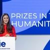 A woman in a red top stands at a podium, presenting at an event titled 'PRIZES IN THE HUMANITIES' organized by the IE Foundation.