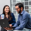 Two people are engaged in a friendly conversation while working on a laptop in a bright, modern office space.