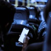 A person using a smartphone on a bus at night, with other passengers visible in the background.