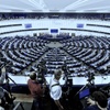 Photographers capturing a session in a large semi-circular parliamentary chamber filled with seated attendees.
