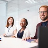 A group of three smiling people at a conference table in a modern office setting.