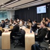 A group of people sitting in a modern classroom listening to a presenter at the front.