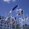 A display of various national flags in front of a modern building under a blue sky with a few clouds.