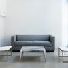 A minimalistic living room with a gray sofa, two white chairs, and a marble table against a backdrop of white walls and large windows.