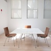 A bright and minimalistic meeting room with a white table, three chairs, and large windows.