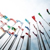 A collection of various national flags fluttering on poles against a blue sky with white clouds.